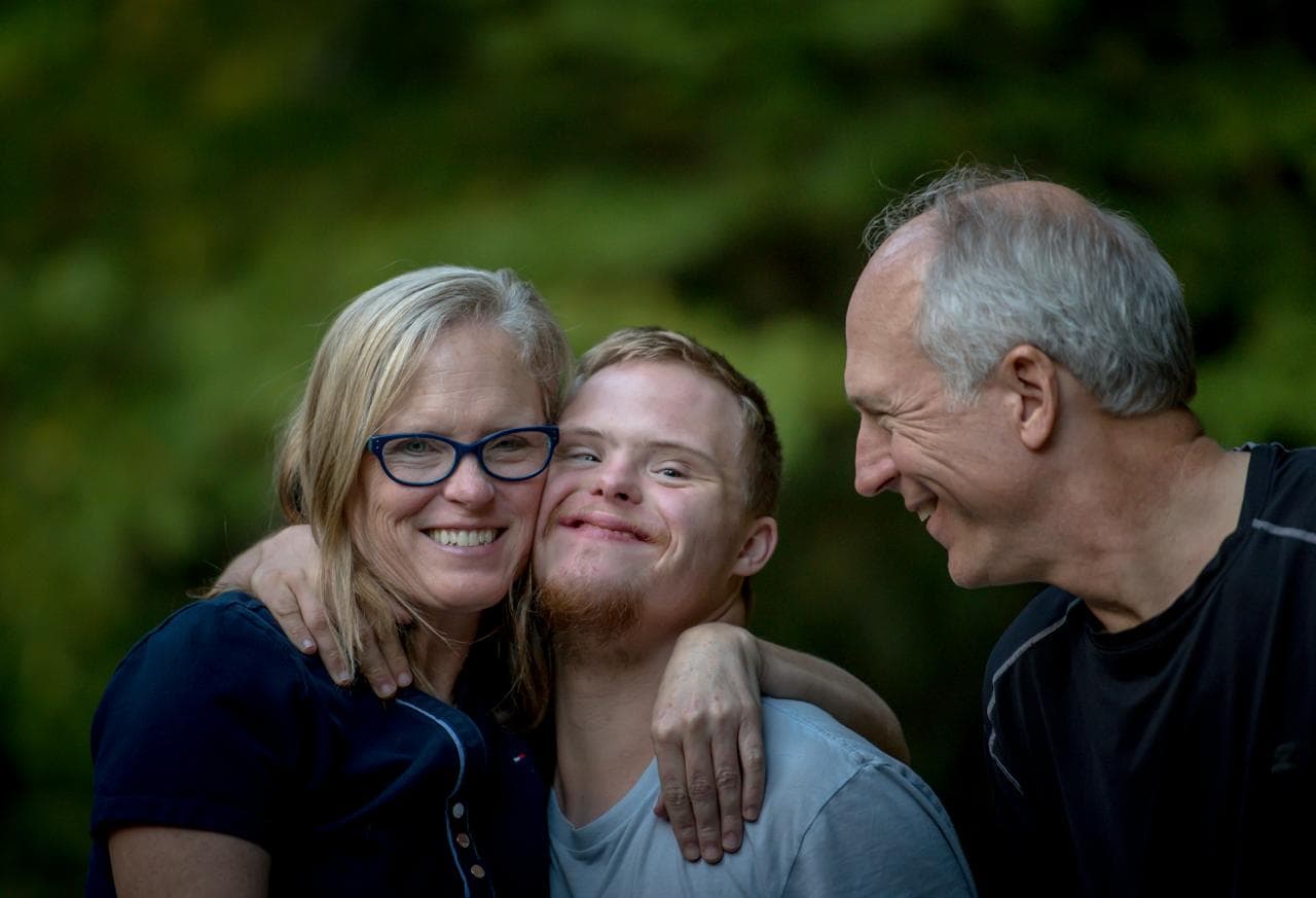 A young man smiling between two older family members outdoors.
